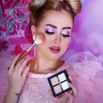 Home Vibrant portrait of a woman applying makeup with a pink theme and elegant hairstyle.
